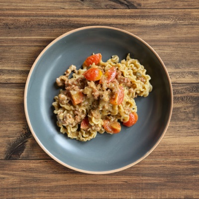 Twisted alisanzas pasta in a creamy sauce with sausage crumbles and cherry tomato pieces in a dark bowl